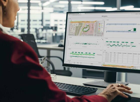 Professional woman sitting at her desk, focused on a computer screen displaying the TEMS Cloud Analytics dashboard with charts and data visualizations