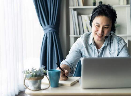 Asian guy with headset and laptop working remotely
