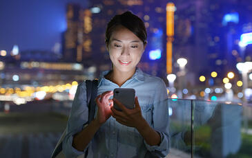 Woman looking at her phone in a dense city at night