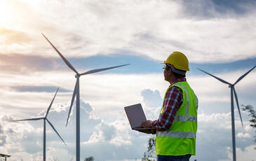 Engineering man standing holding laptop looking at wind turbines