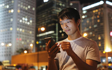Young Asian man using mobile phone in city at night