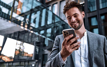 Portrait of modern man in gray suit standing outside office building holding a phone