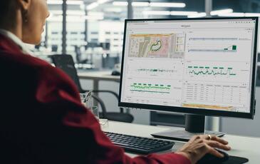 Professional woman sitting at her desk, focused on a computer screen displaying the TEMS Cloud Analytics dashboard with charts and data visualizations