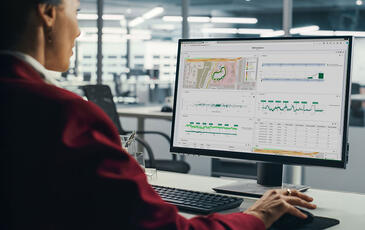 Professional woman sitting at her desk, focused on a computer screen displaying the TEMS Cloud Analytics dashboard with charts and data visualizations