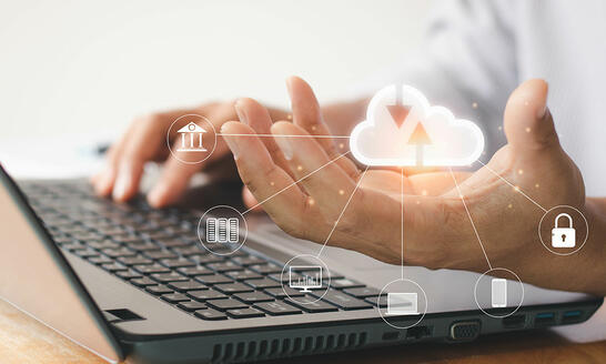 Abstract image of person holding technology cloud while working on laptop