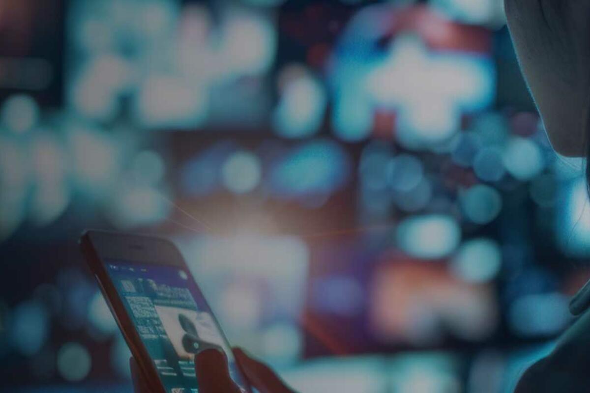 Woman watching streaming video or movies with smartphone in front of wide monitor display computer