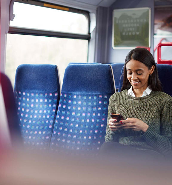 Female Passenger Sitting In Train Looking At Mobile Phone