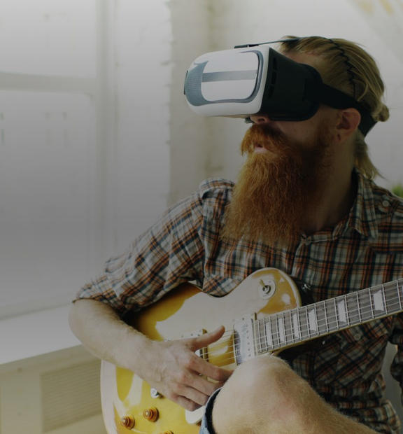 Man with large beard wearing VR glasses while playing guitar