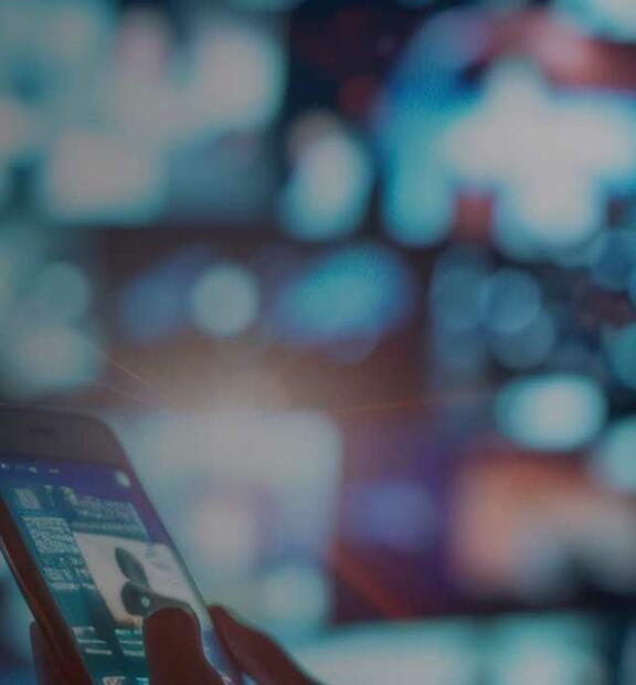 Woman watching streaming video or movies with smartphone in front of wide monitor display computer