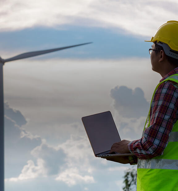 Engineering man standing holding laptop looking at wind turbines