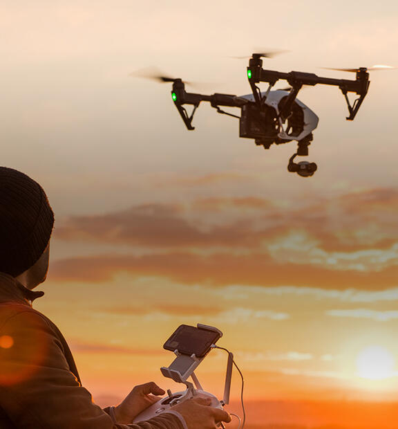 Man operating a drone with remote control. Dark silhouette against colorful sunset