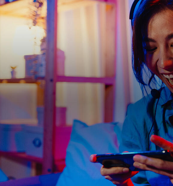 Happy Asian girl gamer wearing headphones, playing a video game on her smartphone