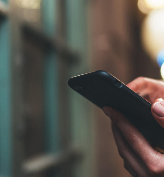 Closeup of a woman standing by a window holding her phone in a dense city at night