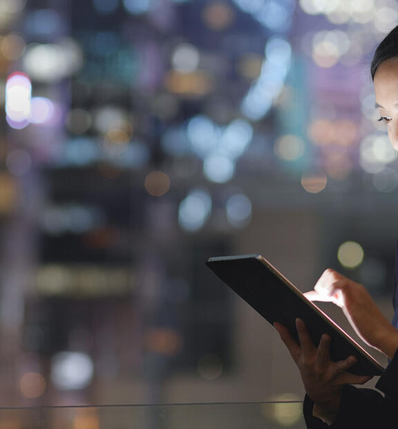 Asian businesswoman in a bustling city at night, using a tablet with city lights glowing around her