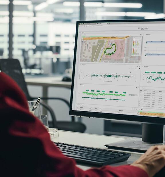 Professional woman sitting at her desk, focused on a computer screen displaying the TEMS Cloud Analytics dashboard with charts and data visualizations