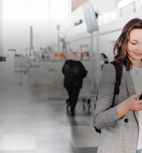 Woman traveler with a backpack standing in an airport terminal, looking at her phone