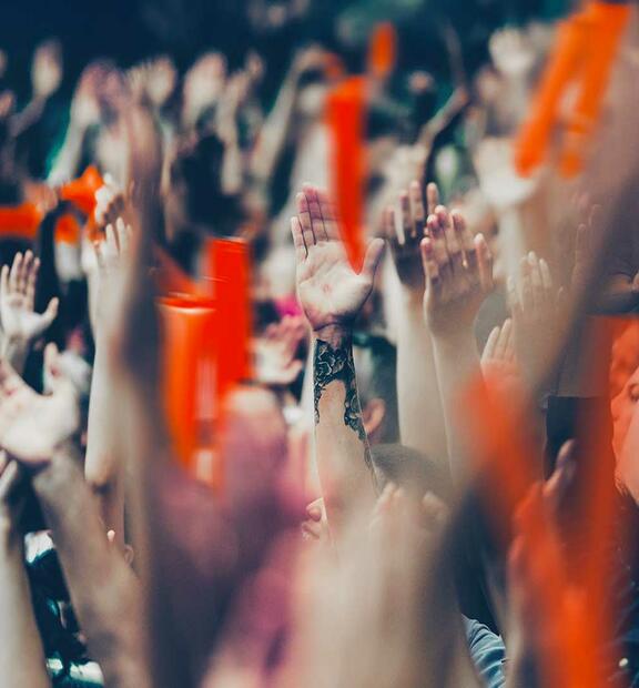 Large crowd in a stadium cheering for their team with their hands raised and clapping.