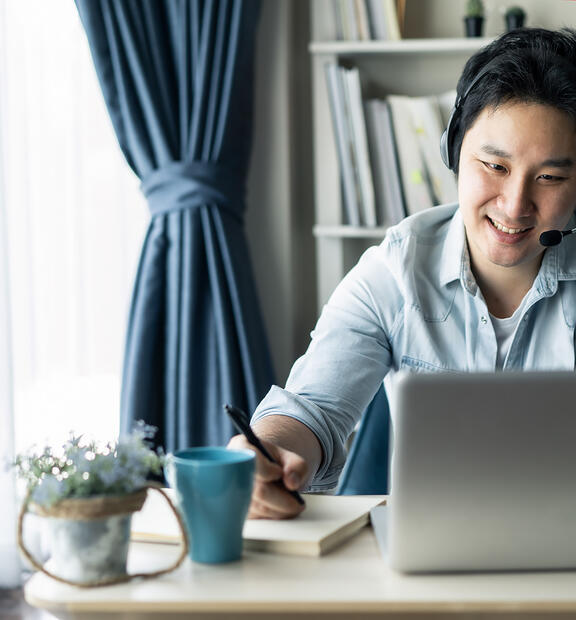 Asian guy with headset and laptop working remotely