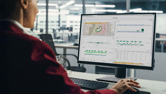 Professional woman sitting at her desk, focused on a computer screen displaying the TEMS Cloud Analytics dashboard with charts and data visualizations
