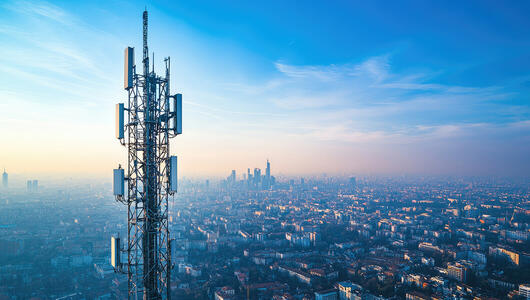 5G telecommunication tower with cityscape backdrop under a blue sky, highlighting 5G network infrastructure and coverage.