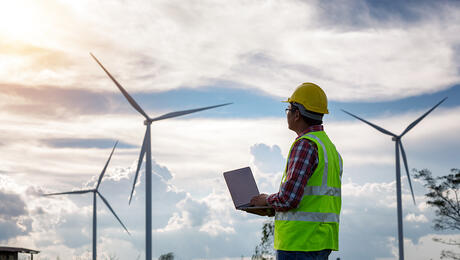 Engineering man standing holding laptop looking at wind turbines