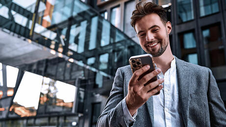 Portrait of modern man in gray suit standing outside office building holding a phone