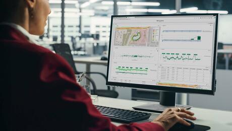 Professional woman sitting at her desk, focused on a computer screen displaying the TEMS Cloud Analytics dashboard with charts and data visualizations